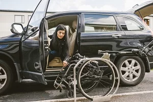 Niepełnosprawna kobieta wysiadająca z samochodu na wózek